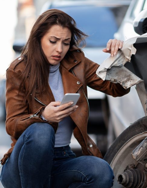 Young sad woman text messaging on smart for after a car crash on the road.