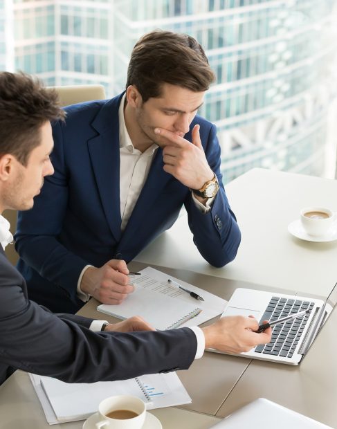 Business partners using laptop while working together on important corporate project in office. Businessman attentively listening to adviser Investment specialist making presentation of promising deal
